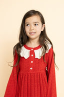 Close up portrait of girl wearing red knit dress with cream scalloped collar and heart buttons, tan background
