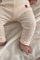 Close up of baby's legs in cream pointelle leggings with strawberry embroidery and red scalloped cuffs