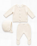 A three-piece baby knit set in cream/off-white, including a long-sleeve button-front cardigan, a bonnet, and footed pants in pure cashmere laid out on a white background.
