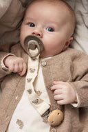 Baby wearing beige knit cardigan holding a pacifier clip with teddy bear embroidered strap and wooden clip