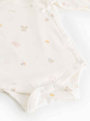 Close up of cream kimono onesie snap closures and tiny toy print detail, flat lay