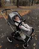 Baby wearing cream hooded jumpsuit with small car print in stroller on leaf covered path