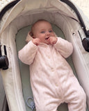 Baby wearing pink floral quilted duvet suit with hood, lying in a stroller bassinet smiling