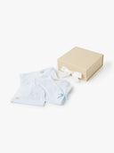 Light blue kimono style wrap romper and hat folded next to an open beige gift box with white ribbon