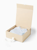 Open beige gift box with light blue kimono style romper folded inside, white ribbon draped over the edge