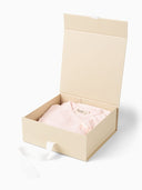 Open beige gift box with pale pink kimono style romper folded inside, white ribbon draped over the edge