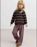 Child wearing brown heart print sweater with pink and brown heather striped pants, standing