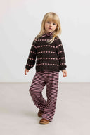 Girl standing wearing dark brown knit sweater with pink heart stripe pattern and matching striped pants, brown boots