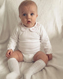 Baby sitting wearing white pointelle knee socks with a floral collared white bodysuit
