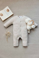 Beige melange wool cashmere romper flat lay with patch pockets, styled with a plush teddy bear teether, dried baby's breath, and an open storybook on linen background