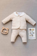 Beige melange cardigan and pants set with embroidered white collar and chest pocket, flat lay styled with a wooden bear teether and seashell illustration card on linen background
