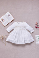 Pearl long sleeve dress with pintuck bodice and gold metallic floral embroidery, flat lay styled with a wooden horse toy, dried baby's breath, and an open storybook on linen background