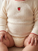 Baby wearing a cream-colored outfit with red trim and a strawberry design.