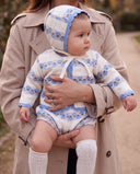 Mother carrying baby wearing cream cardigan and bloomer set with blue floral stripe pattern and matching bonnet, outdoors on a path