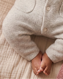Close up of baby feet peeking out from beige melange wool cashmere romper with patch pockets and button placket