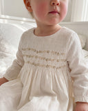 Close up of toddler wearing pearl long sleeve dress with pintuck bodice and gold metallic floral embroidery
